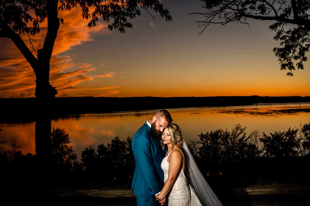 A emotionally-touched bride and groom standing by a lake during their backyard wedding in La Crosse at sunset.