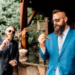 A man in a blue suit is smoking a cigar at an emotional backyard wedding.