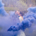 Courtney and James kissing at their love-filled wedding with a blue smoke bomb in the backyard.