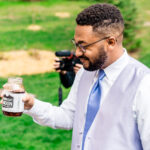 A man is holding a jar of bourbon at Courtney and James' love-filled backyard Trempleau wedding.
