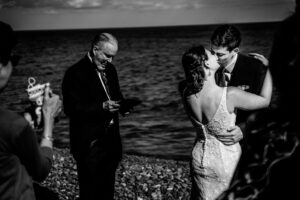 A bride and groom kissing in front of the ocean.
