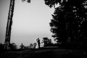 Black and white photo of a bride and groom standing in the woods.