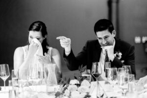 A bride and groom at a table with glasses of wine.