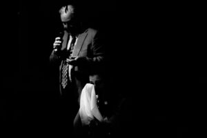 A man in a suit is holding a microphone in the dark.