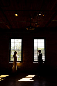 A bride and groom standing in front of a window.