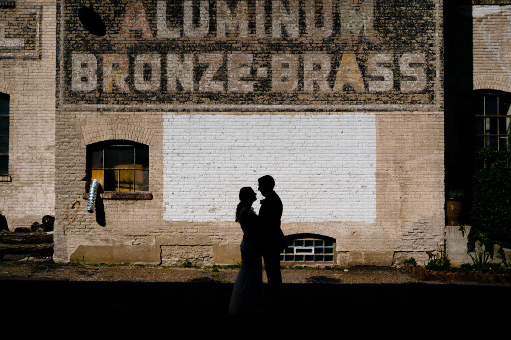 A bride and groom are silhouetted in front of an aluminum bronze brass sign.