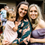 Two women holding a baby in front of a crowd at Courtney and James' love-filled backyard Trempleau wedding.