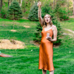 A love-filled wedding ceremony in Courtney and James' backyard featuring a woman in an orange dress standing in the grass.