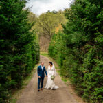 Courtney and James walking down a path in a forest during their love-filled backyard Trempleau wedding.