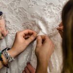 A woman is adding a button to Courtney and James' love-filled backyard Trempleau Wedding dress.