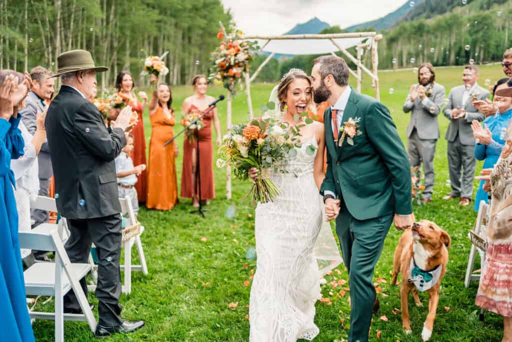 A bride and groom walking down the aisle with their dog.