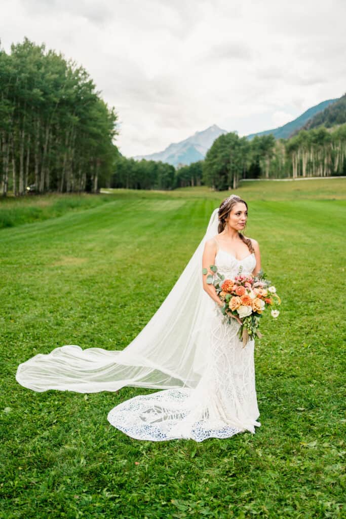 A bride standing in a field with mountains in the background.