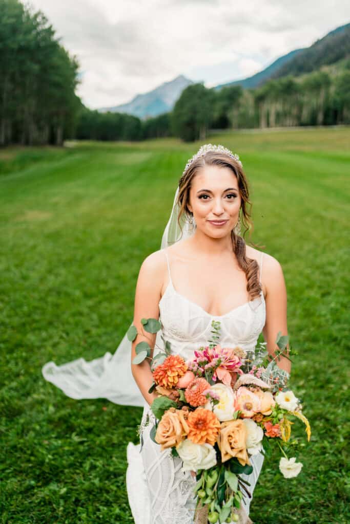 A bride holding a bouquet in a field with mountains in the background.