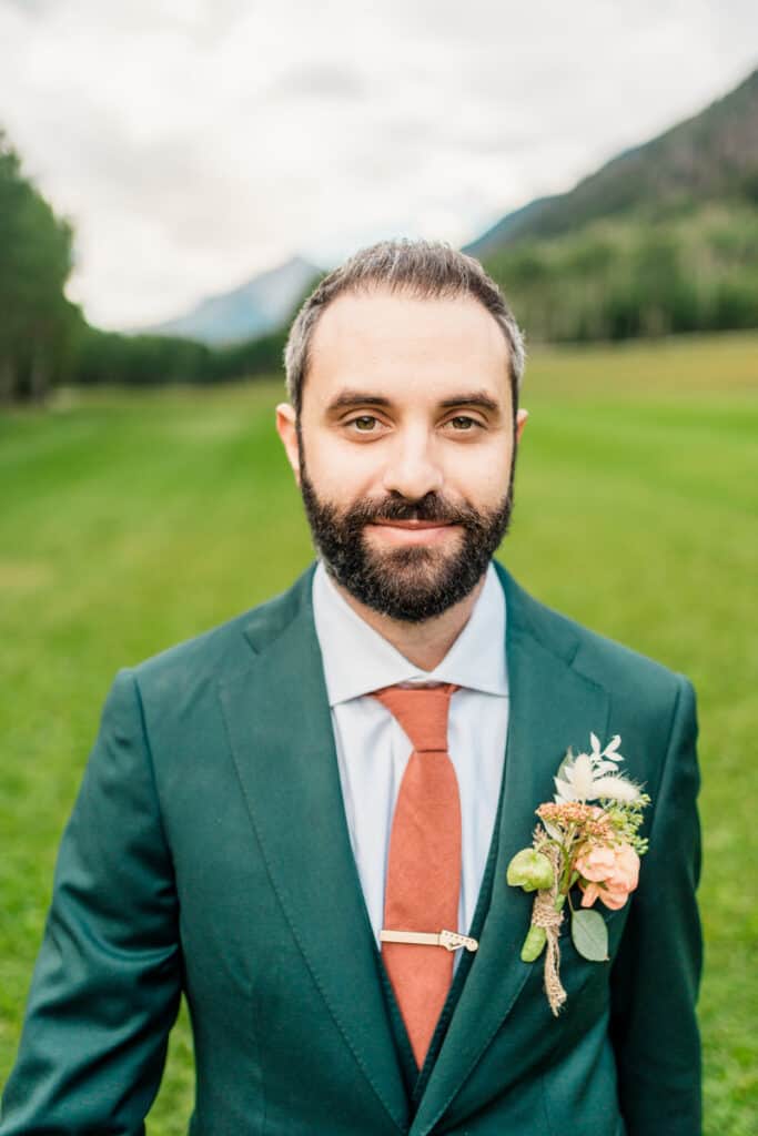 A groom in a green suit and orange tie.