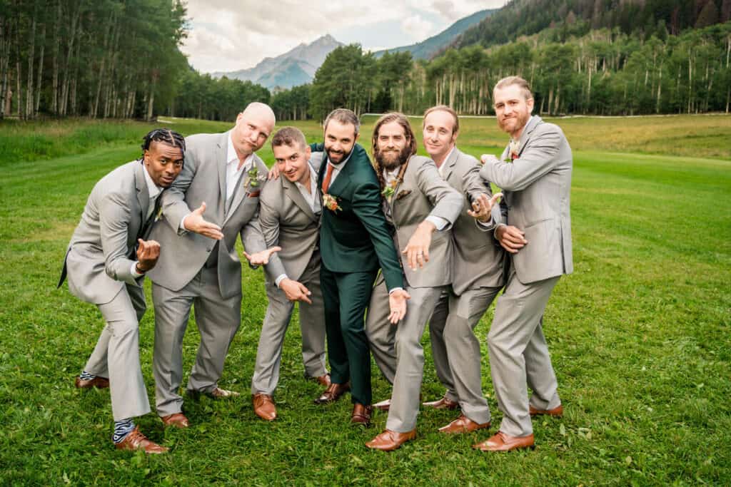 Groomsmen posing for a photo in a field with mountains in the background.