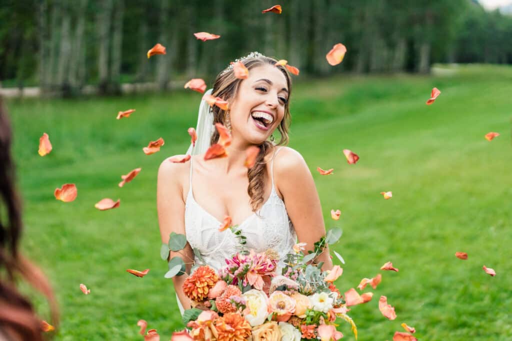 A bride laughs while throwing flowers in the air.