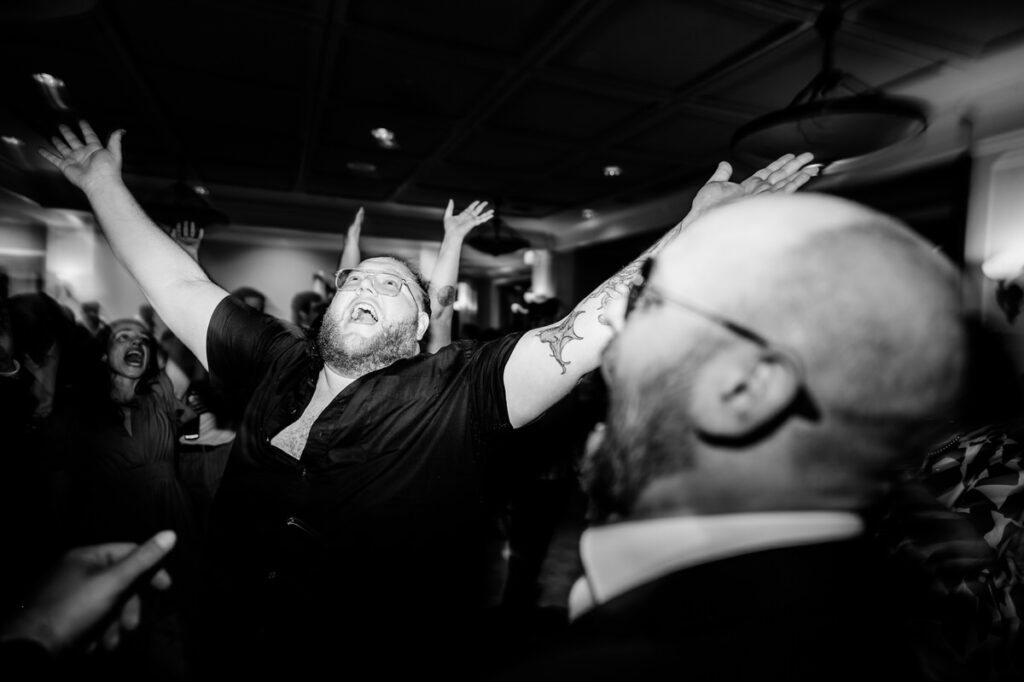 A man with his arms up in the air at a wedding.
