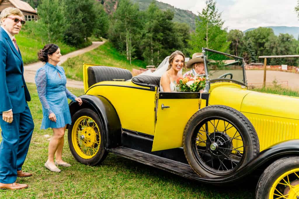 A bride and groom standing next to an antique car.