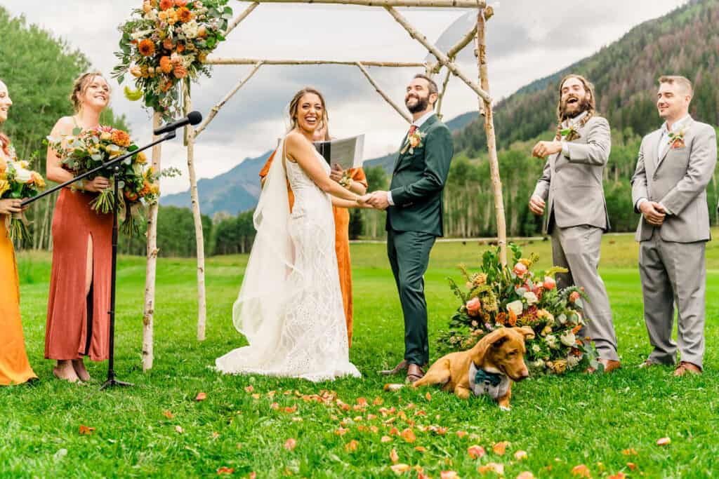 A wedding ceremony in the mountains with a dog in the background.