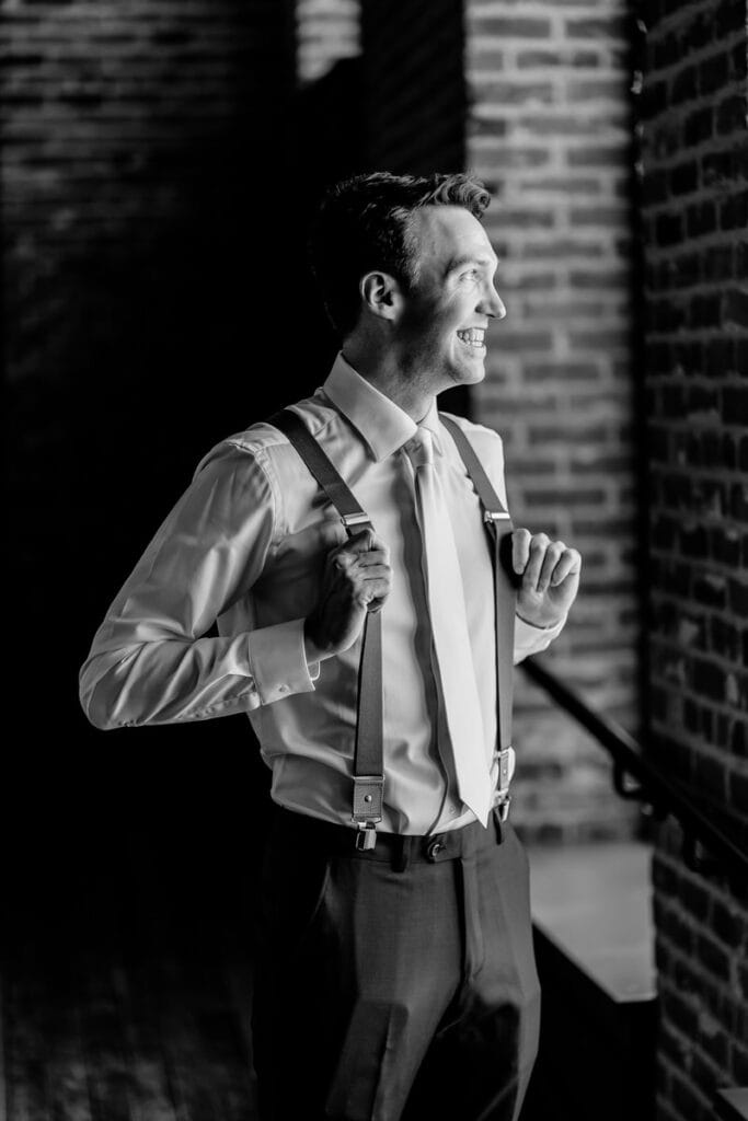 A black and white photo of a groom with suspenders.