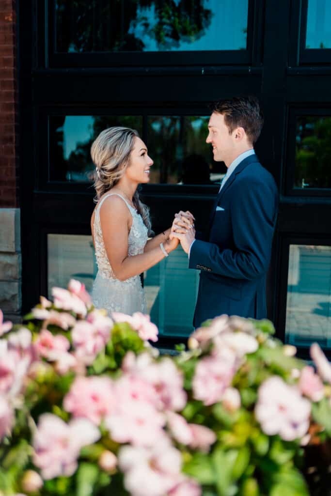 A bride and groom standing in front of a building with flowers.