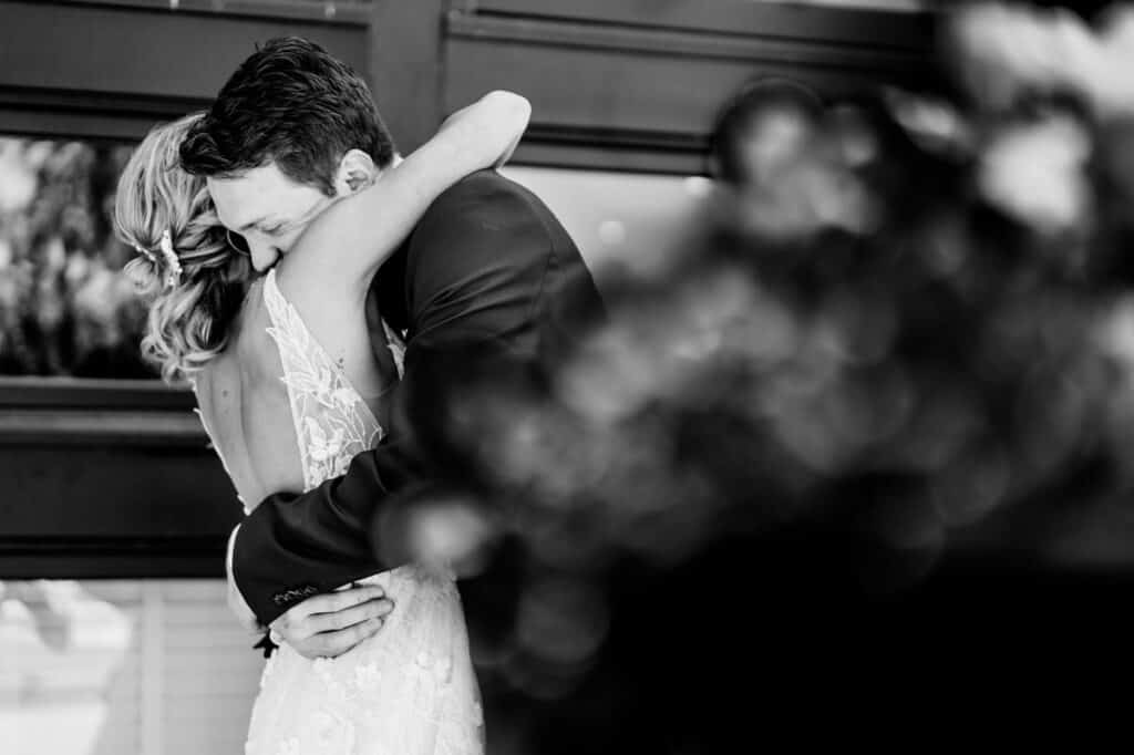 A bride and groom hugging in front of a window.