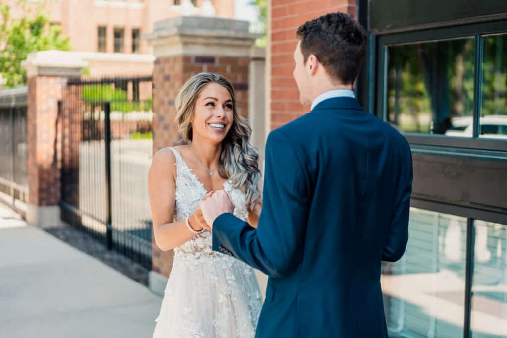 A bride and groom smiling at each other in front of a building.