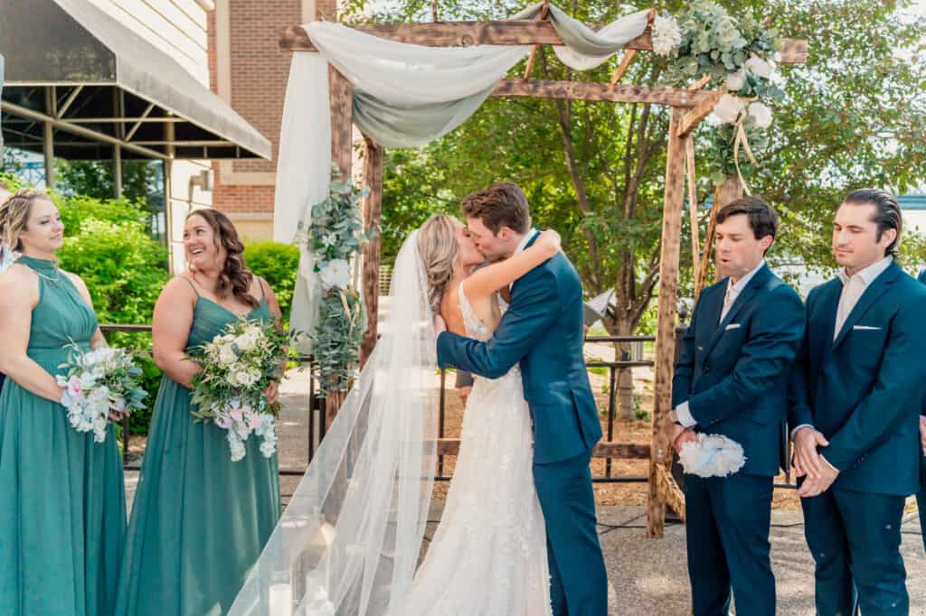 A bride and groom kiss in front of their wedding party.