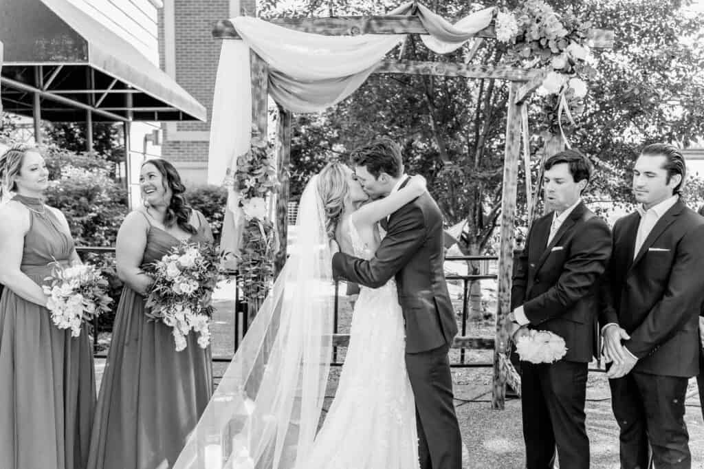 A bride and groom kiss in front of their wedding party.