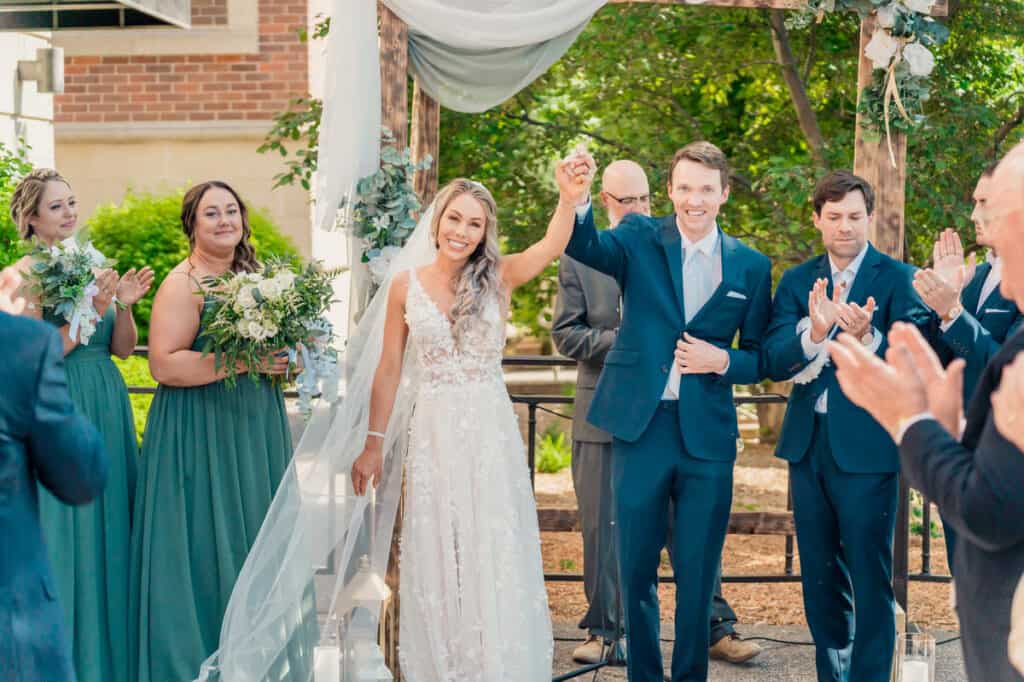 A bride and groom waving at each other during their outdoor wedding ceremony.