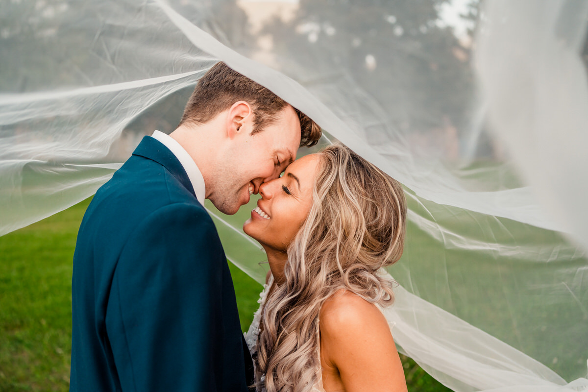 A bride and groom kiss under a veil.