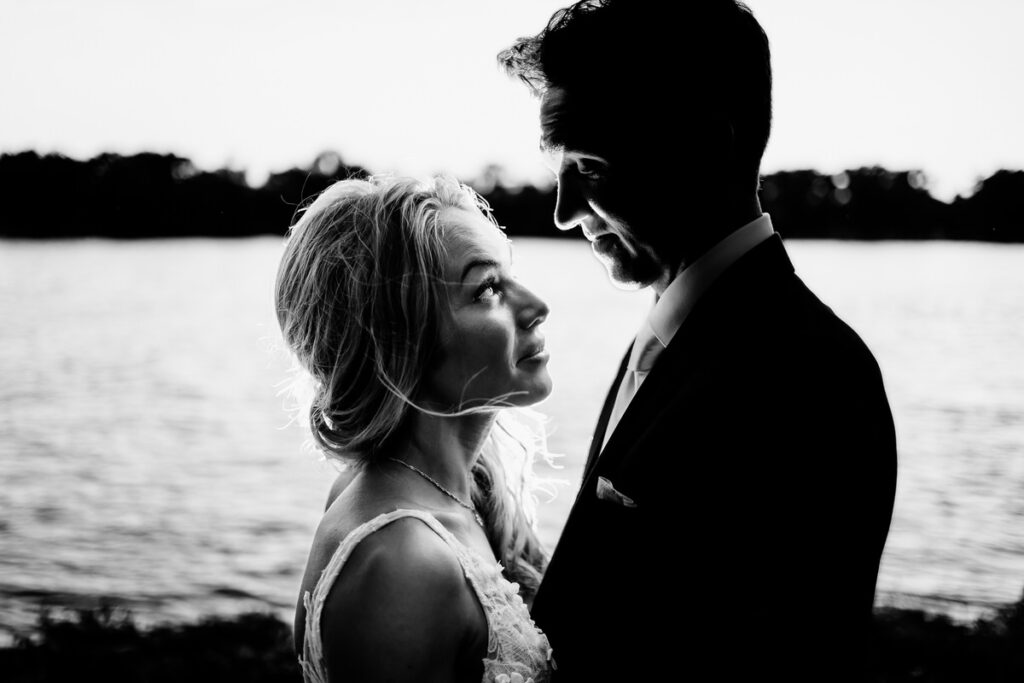 A black and white photo of a bride and groom standing next to a lake.