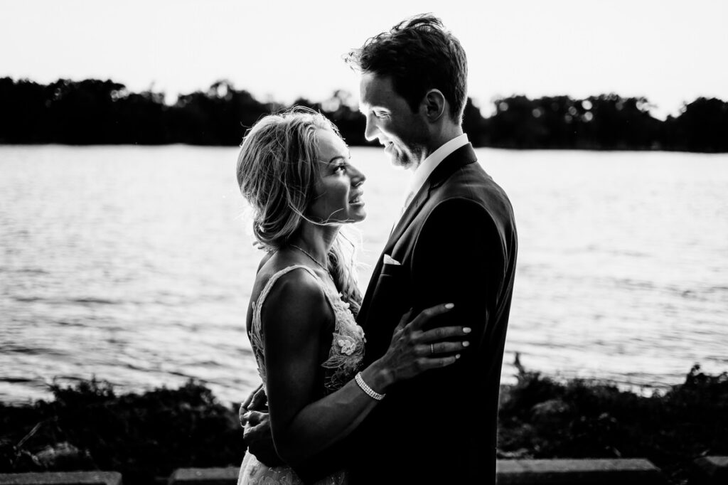 A bride and groom embracing in front of a lake.