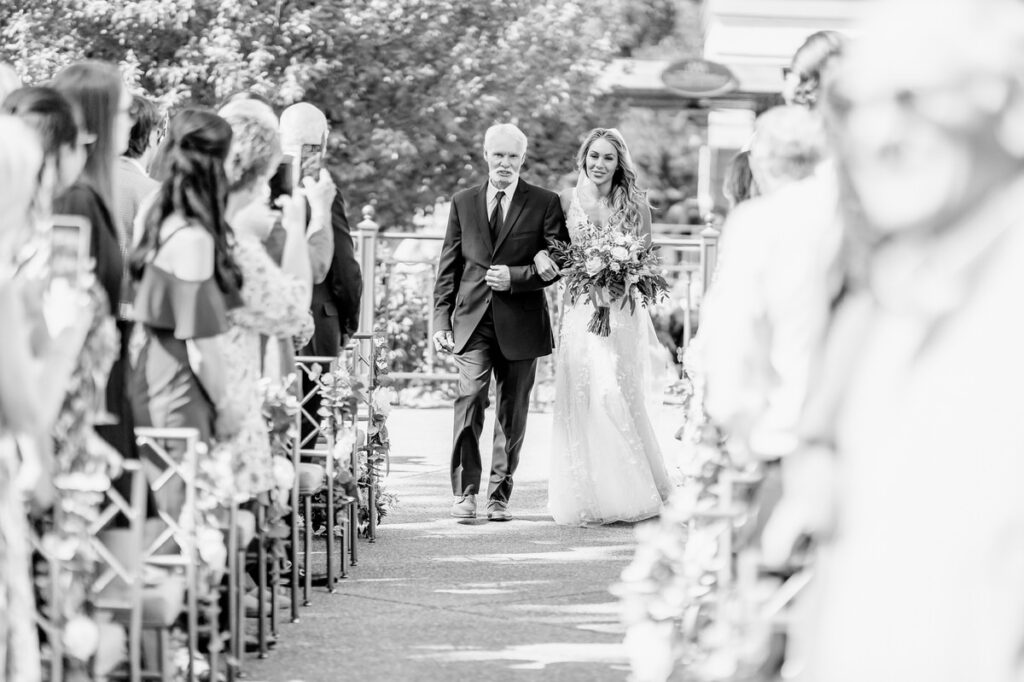 A black and white photo of a bride and her father walking down the aisle.