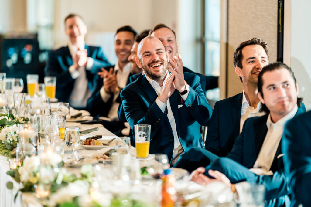 A group of groomsmen clapping at a wedding reception.