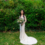 A bride in a white wedding dress standing in front of bushes.