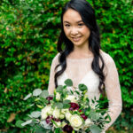 A bride holding a bouquet in front of bushes.
