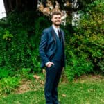 A man in a suit standing in front of a tree.