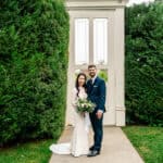 A bride and groom standing in front of a hedge.