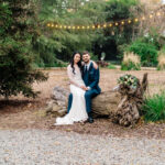 A bride and groom sitting on a log in the woods.