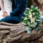 A bride and groom sitting on a log in the woods.