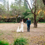A bride and groom walking through a wooded area.