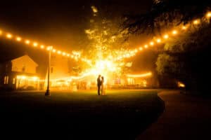 A couple standing under a tree at night.