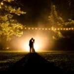 A bride and groom standing in a field at night.