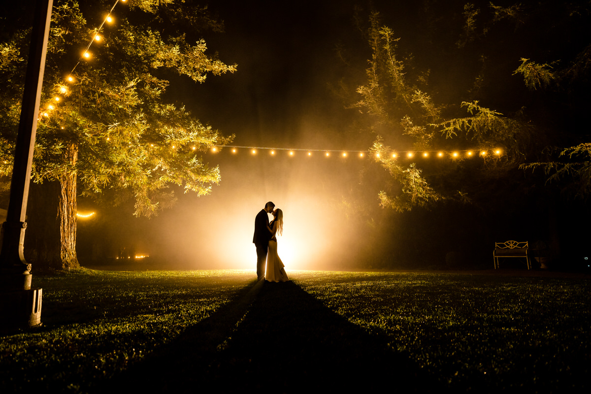 A bride and groom standing in a field at night.