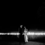A bride and groom standing in front of a fountain at night.