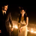 A bride and groom standing in front of a fire pit.