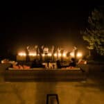 A group of people standing around a fire pit at night.