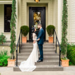 A bride and groom standing on the steps of a mansion.