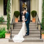 A bride and groom kiss on the steps of their home.